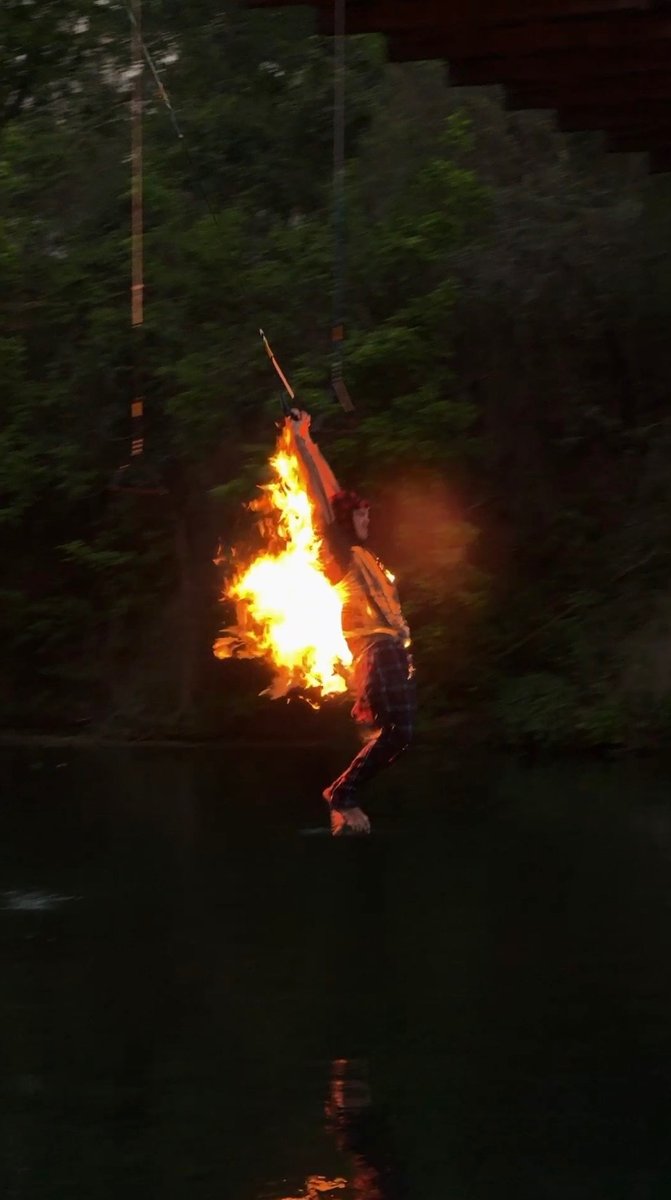 Joe on a flaming rope swing over water at dusk