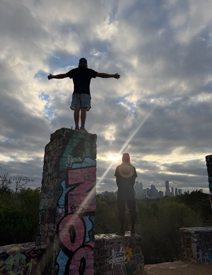 Joe atop a graffiti pillar at sunrise, Austin skyline behind him